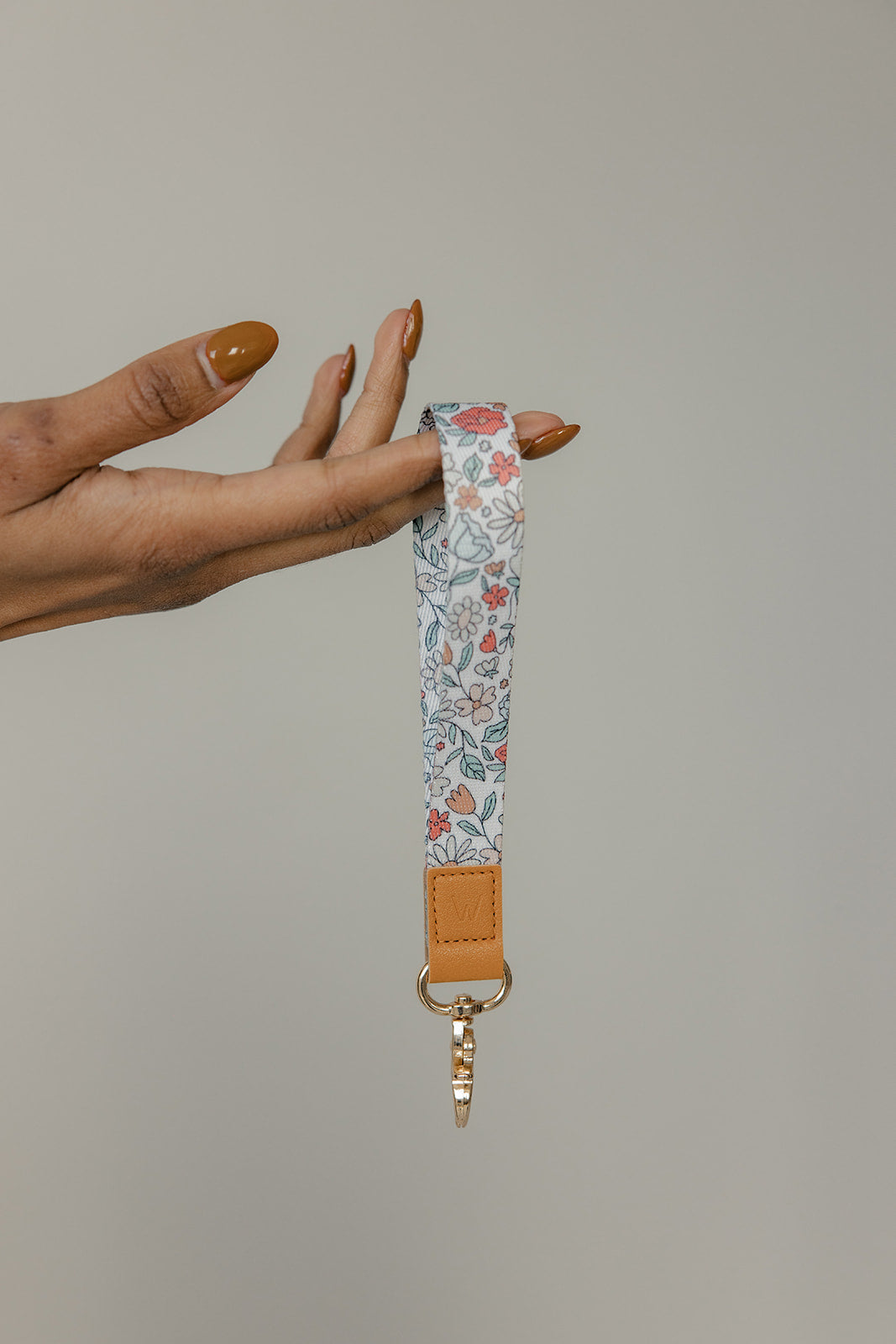 Floral wrist lanyard with tan leather strap and gold clasp, fabric tie at end.