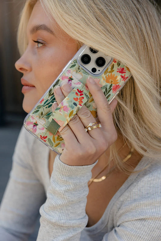 Floral phone case on a hand, showing clear sides and a green strap across the back.