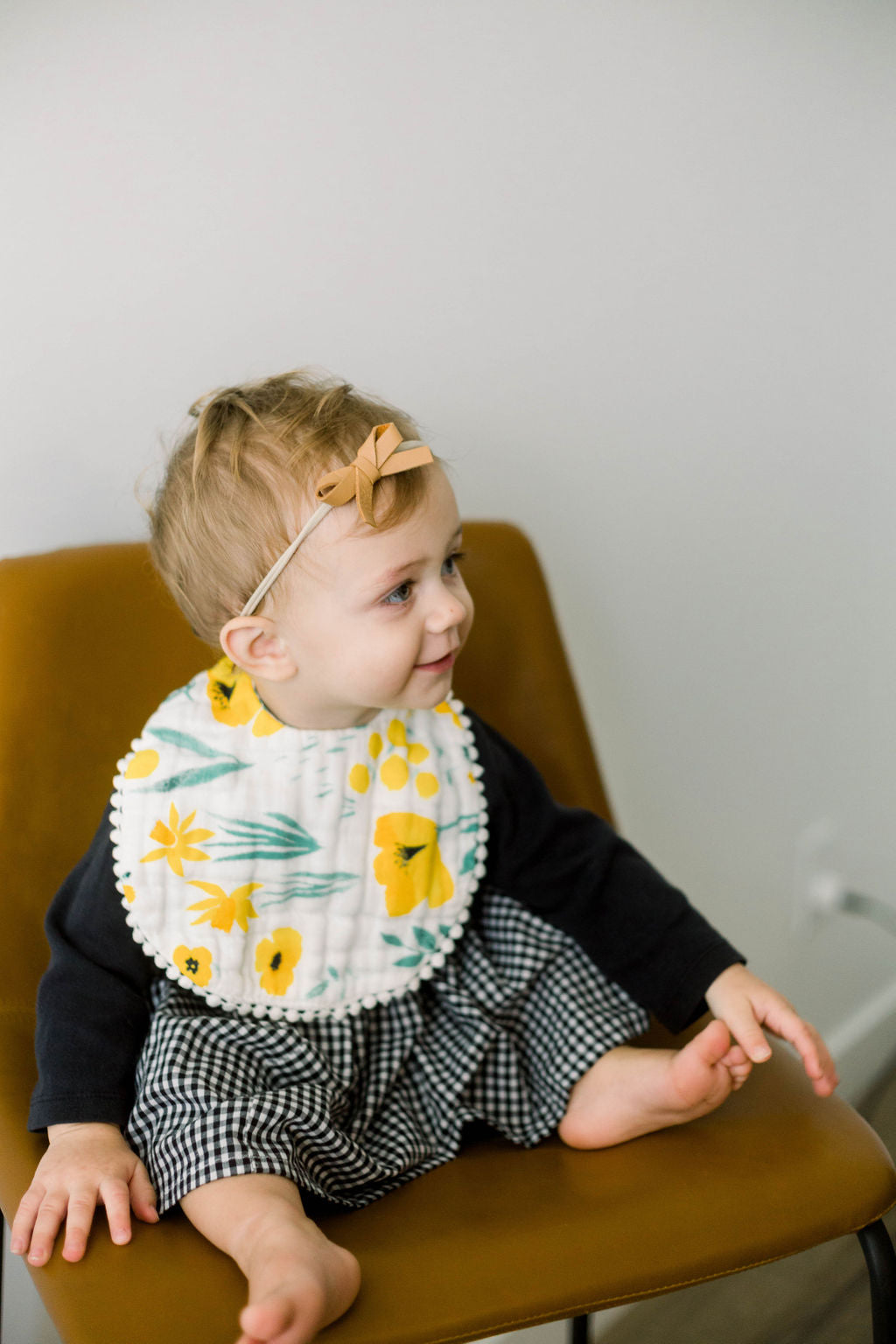 Baby wearing yellow floral bib with scalloped edges and neck tie, seated and smiling