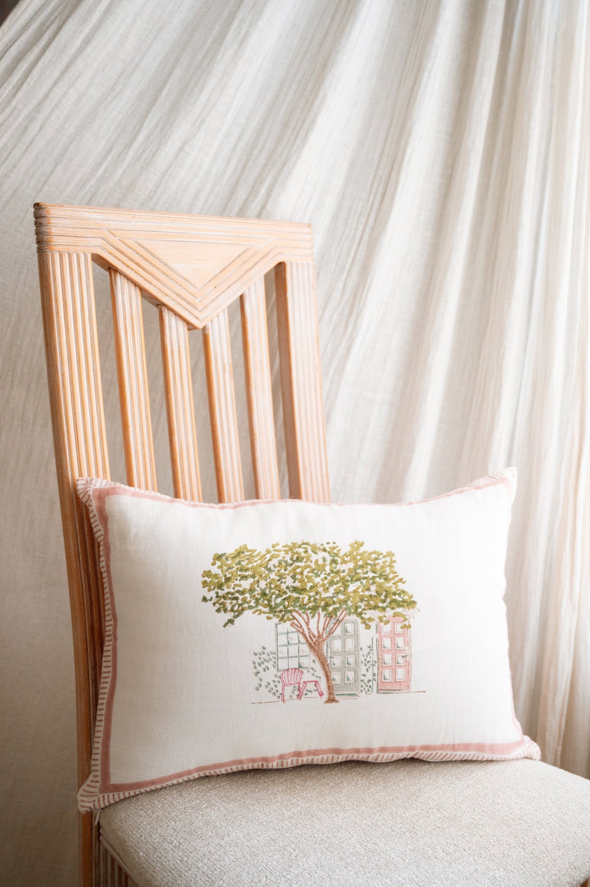 Block print cushion with tree-and-house print and pink trim on chair backrest