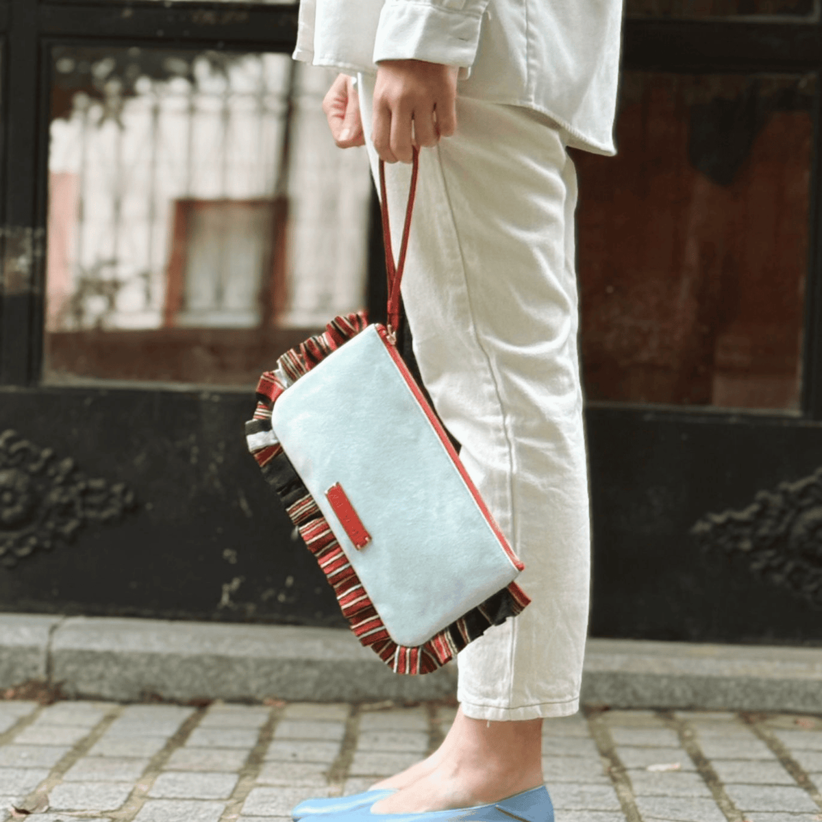 Light blue denim clutch bag with red crossbody strap and striped trim lining