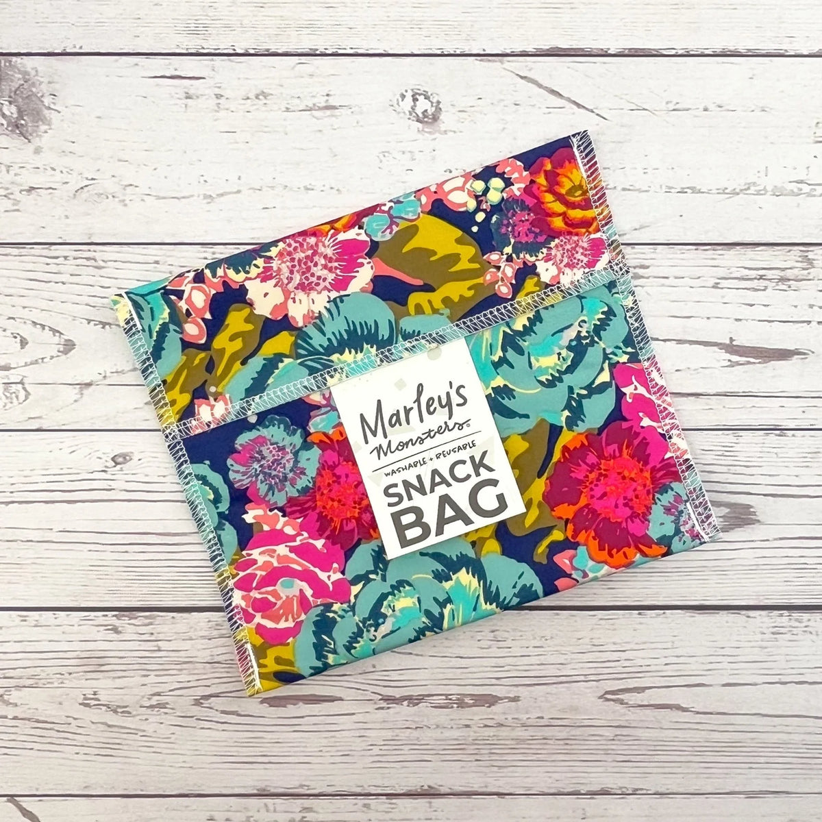 Reusable snack bag with colorful tropical floral print on teal fabric, sealed top flap.
