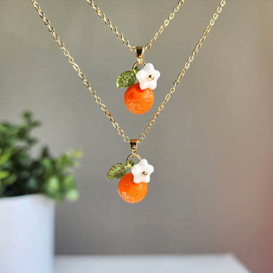 Gold-tone orange fruit charm necklace with two layered charms and green leaves