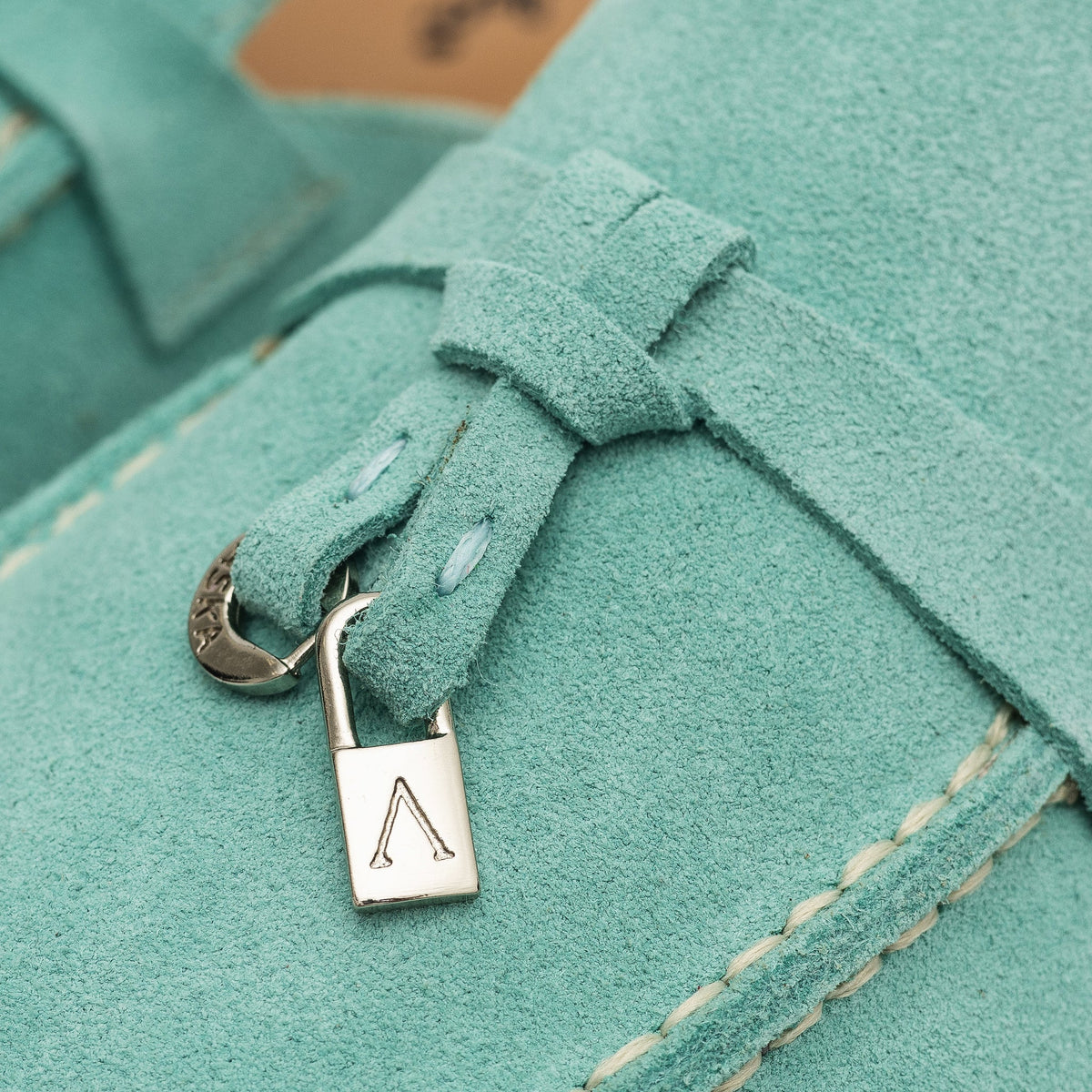 Close-up of turquoise suede mule tassel with metal hardware and moc stitching