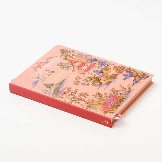 Hardcover chinoiserie notebook lying open, showing pink cover and red-edged spine