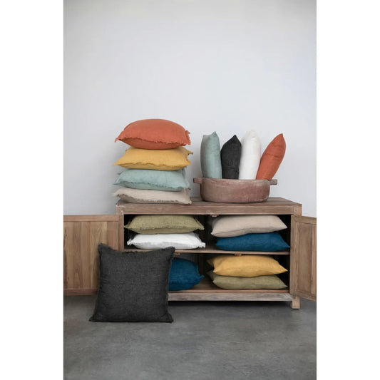 Assorted decorative pillows in muted colors, stacked on a wooden cabinet