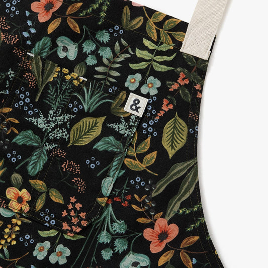 Floral apron with stitched beige crossback straps and woven logo patch