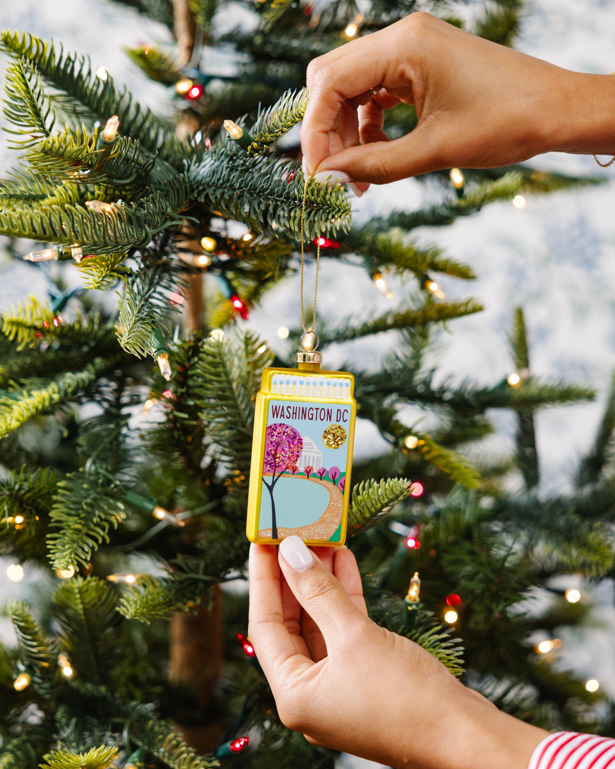 Washington DC matchbook ornament on gold cord being placed on a tree