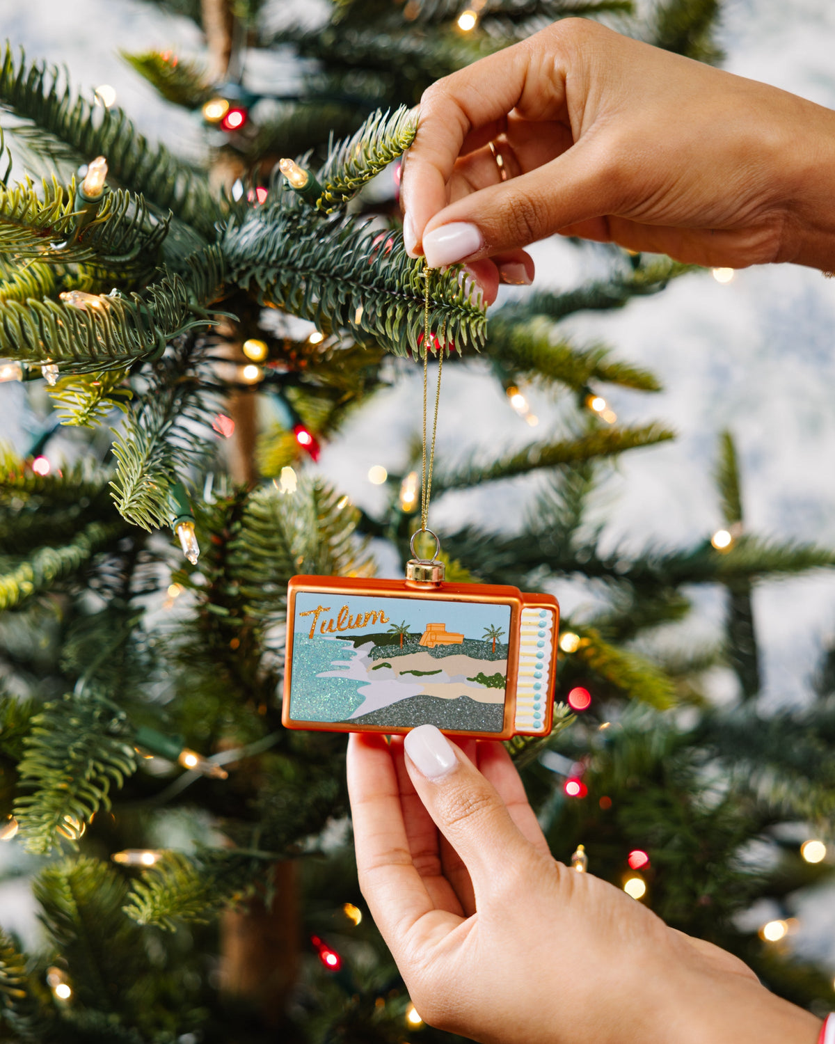 Tulum matchbook ornament held by hands, orange frame, gold-capped hanging cord