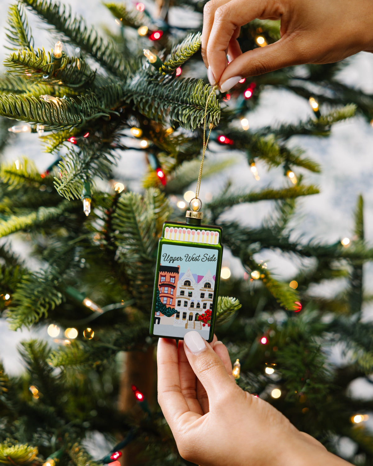 Hand placing matchbook ornament on pine branches, gold cord and Upper West Side artwork