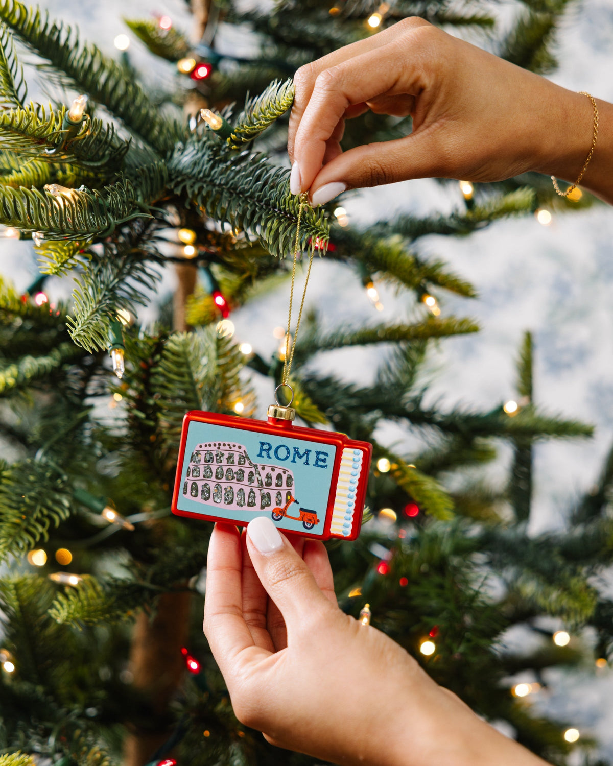 Rome matchbook ornament clipped onto a Christmas tree branch by hands