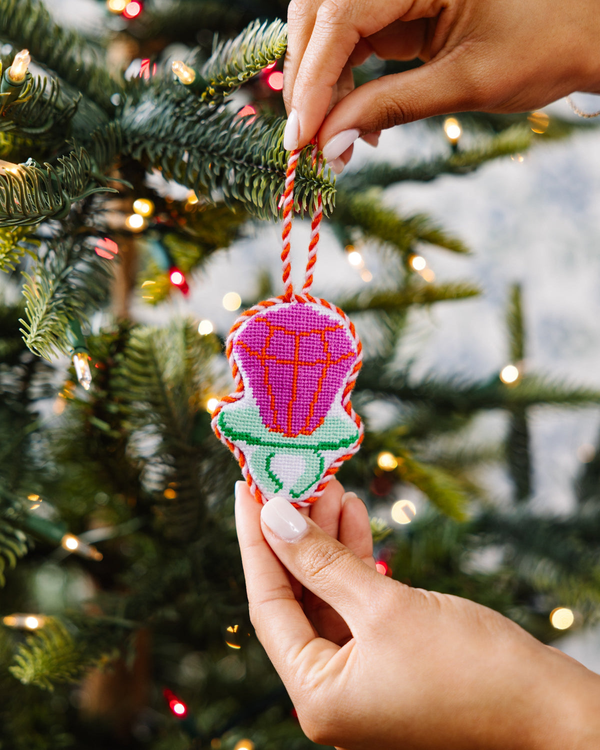 Needlepoint candy ring ornament being hung, pink-purple candy with green base on cord