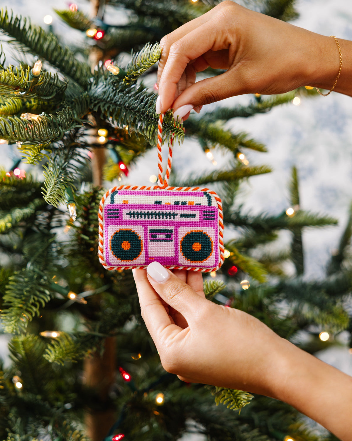 Needlepoint boom box ornament being hung on a Christmas tree branch