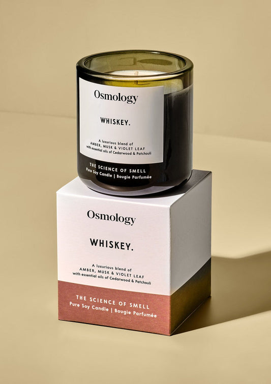 Scented candle in dark glass jar with label, shown beside matching gift box