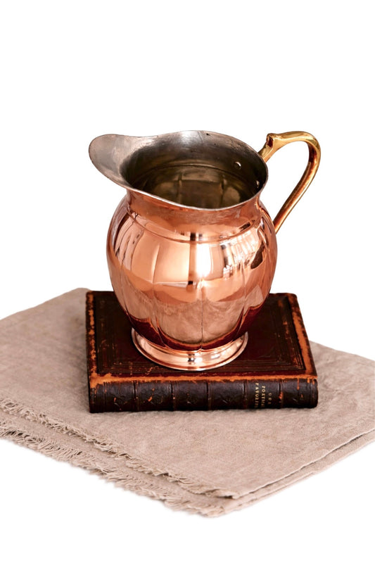 Copper metal pitcher with curved handle, flared spout, and reflective interior.