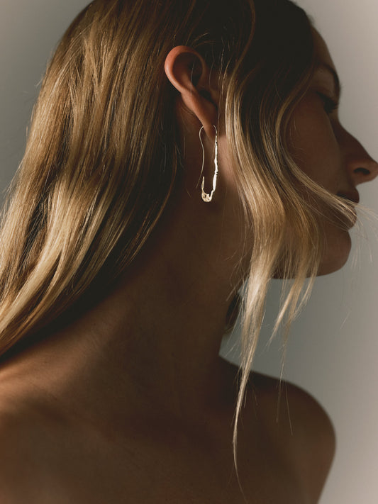 Gold paperclip hoop earrings on ear, elongated wavy link drop