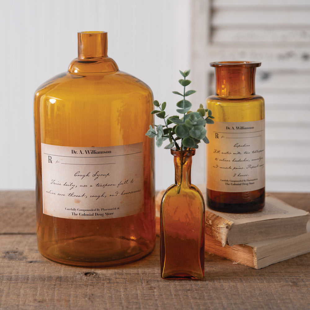 Large amber apothecary bottle with bronze cap and script label, plus matching smaller bottle.