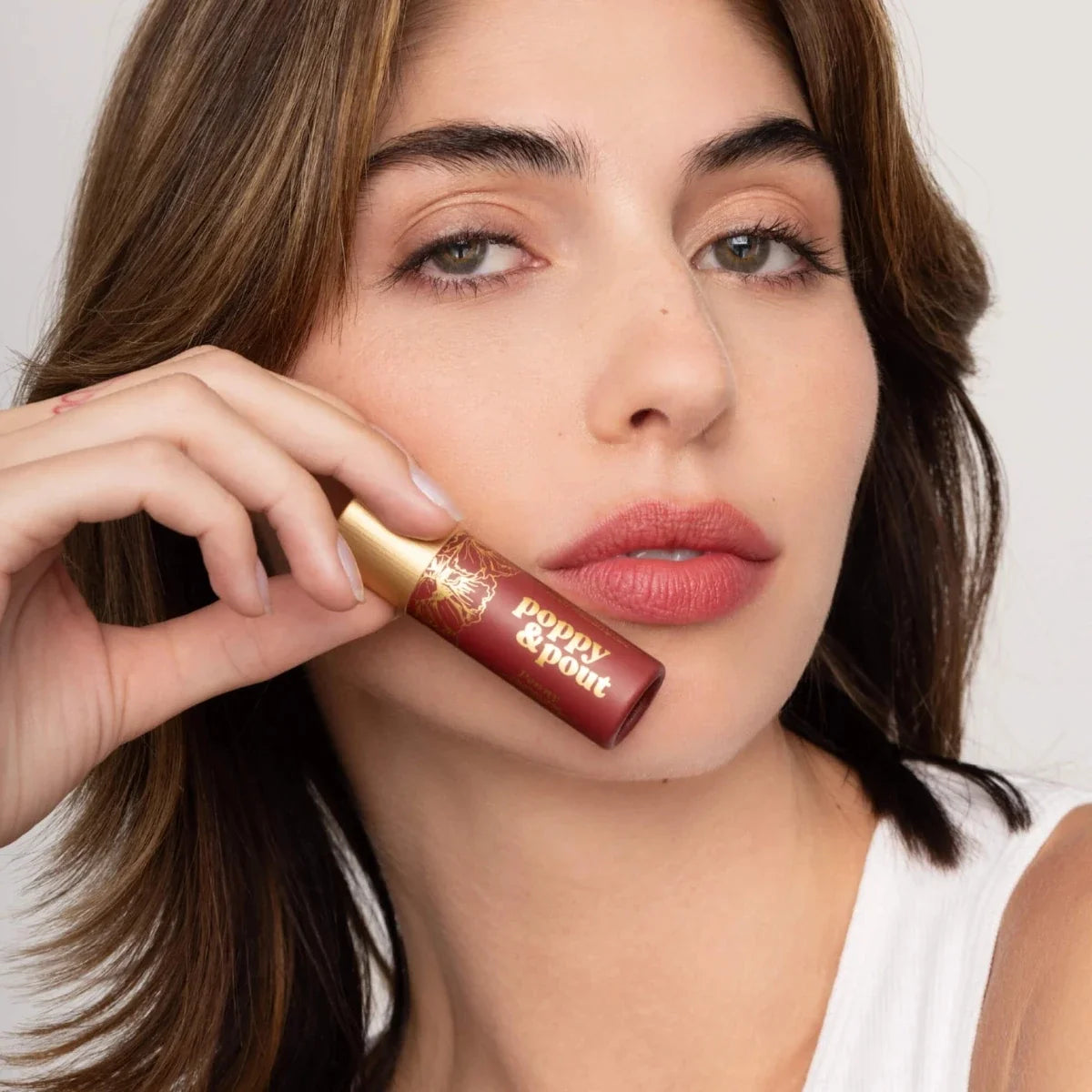 Lip tint tube with gold cap near lips, rosy red shade