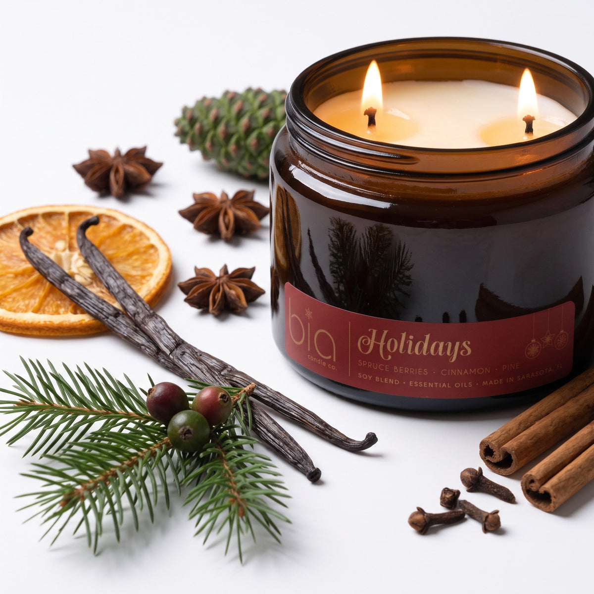 Amber glass soy candle jar with two flames and holiday label, with pine needles and spices
