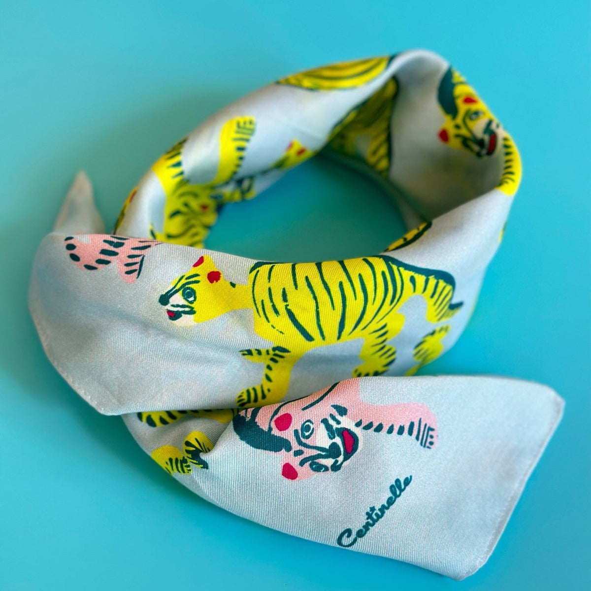 Folded light-blue bandana with yellow tiger print and colorful accents.