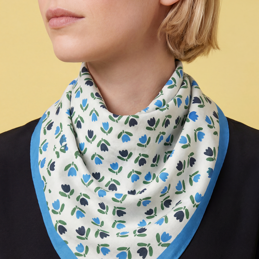 Tulip-print cotton bandana draped around neck with blue edge trim.