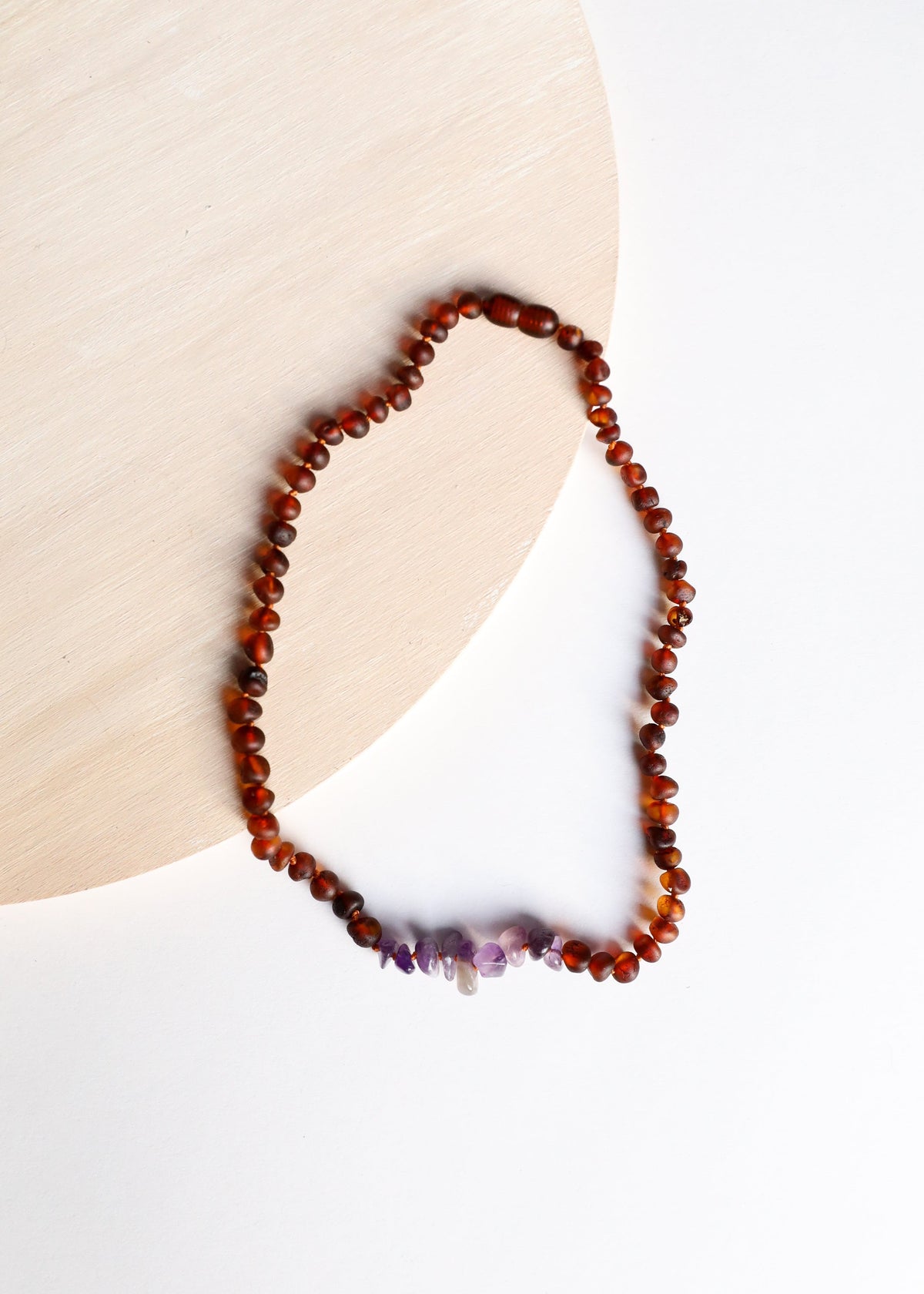 Amber beaded heart-shaped necklace with purple amethyst points, partial view.