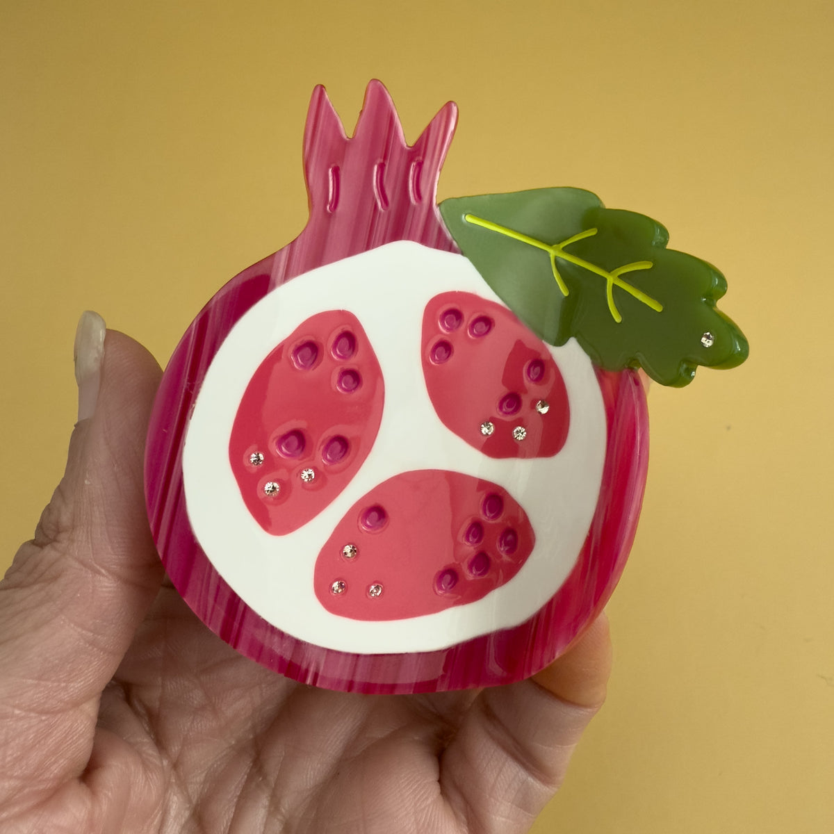 Pomegranate-themed hair claw held in hand, red fruit design with glitter rhinestone dots