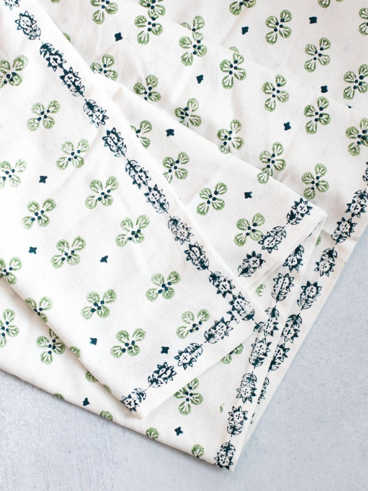 Ivory table throw with green clover print and dark blue striped border, folded corner