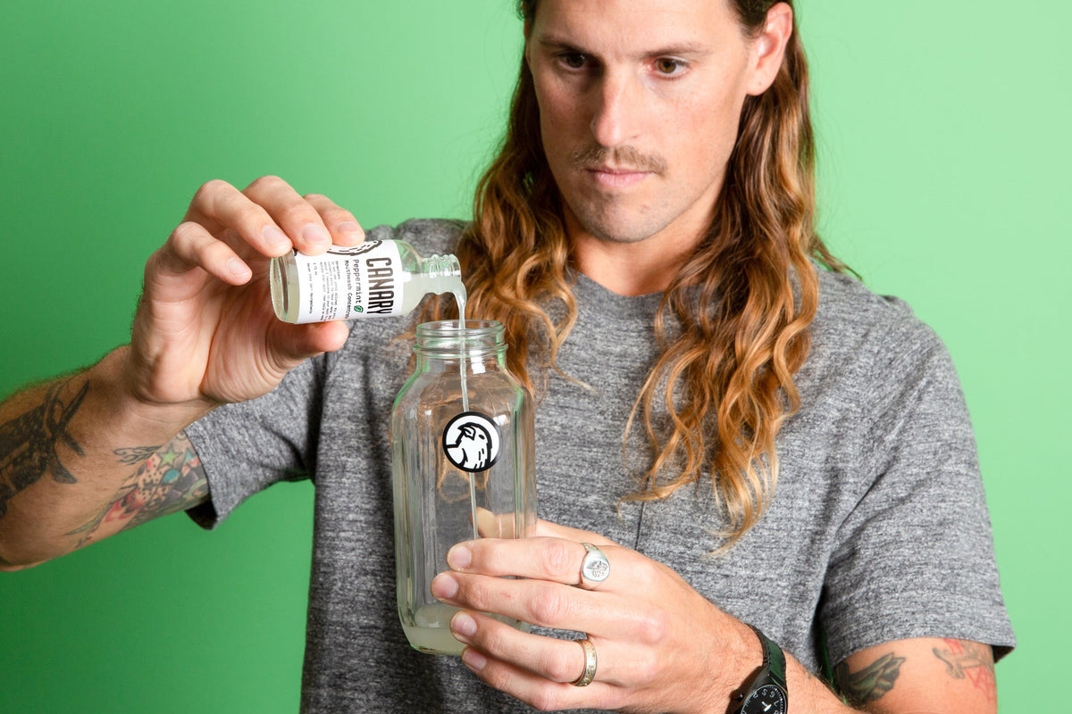 Peppermint mouthwash concentrate poured from a small bottle into a glass jar
