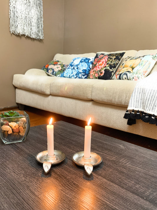 Two silver taper candlestick holders with leaf handles, holding lit tapers