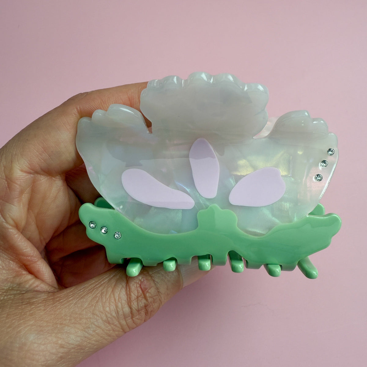 Opalescent floral hair claw with green base and rhinestones, held in hand for size