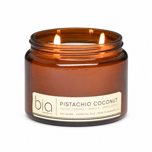 Amber glass candle jar with lit wicks, “Pistachio Coconut” label