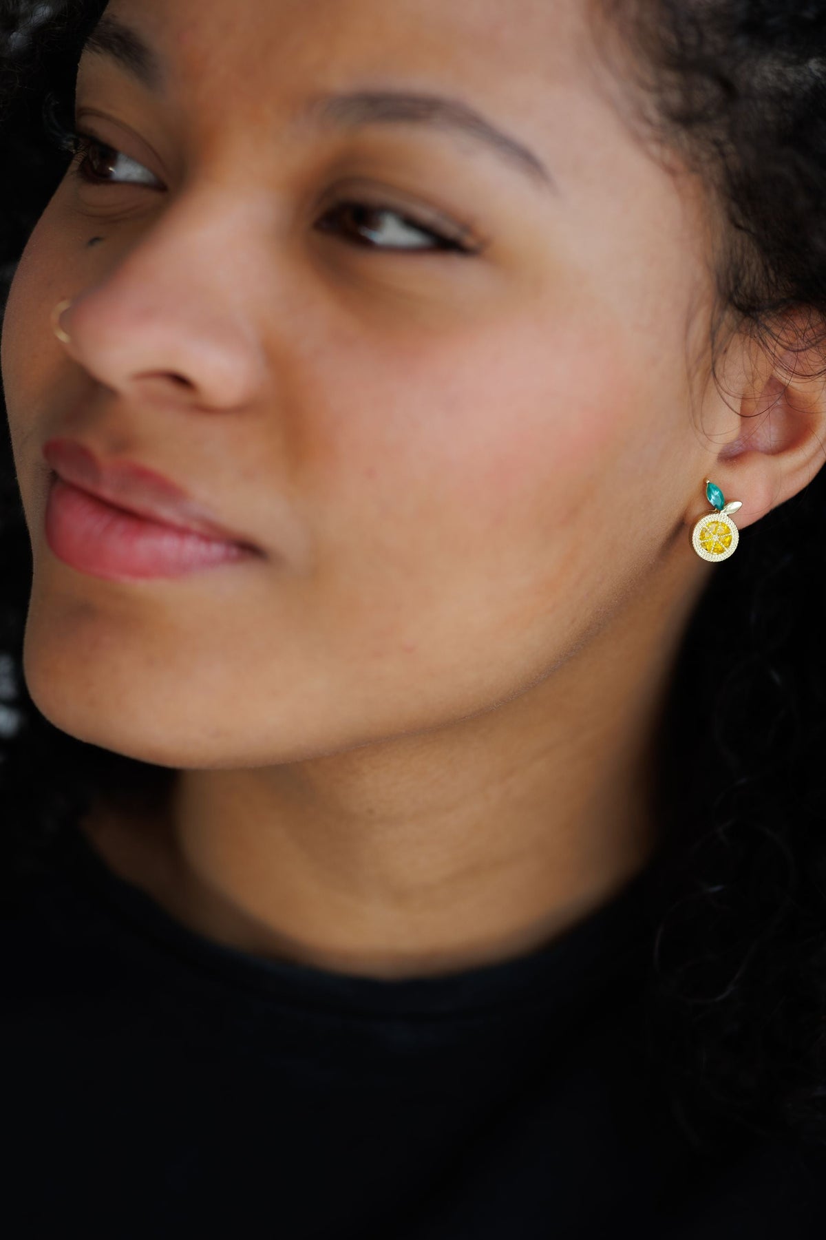 Lemon stud earring on model: gold textured round charm with teal top and green leaf detail