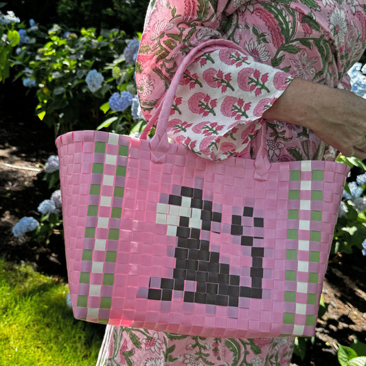 Pink woven basket bag with green check sides and pixel-style monkey face, held by hand