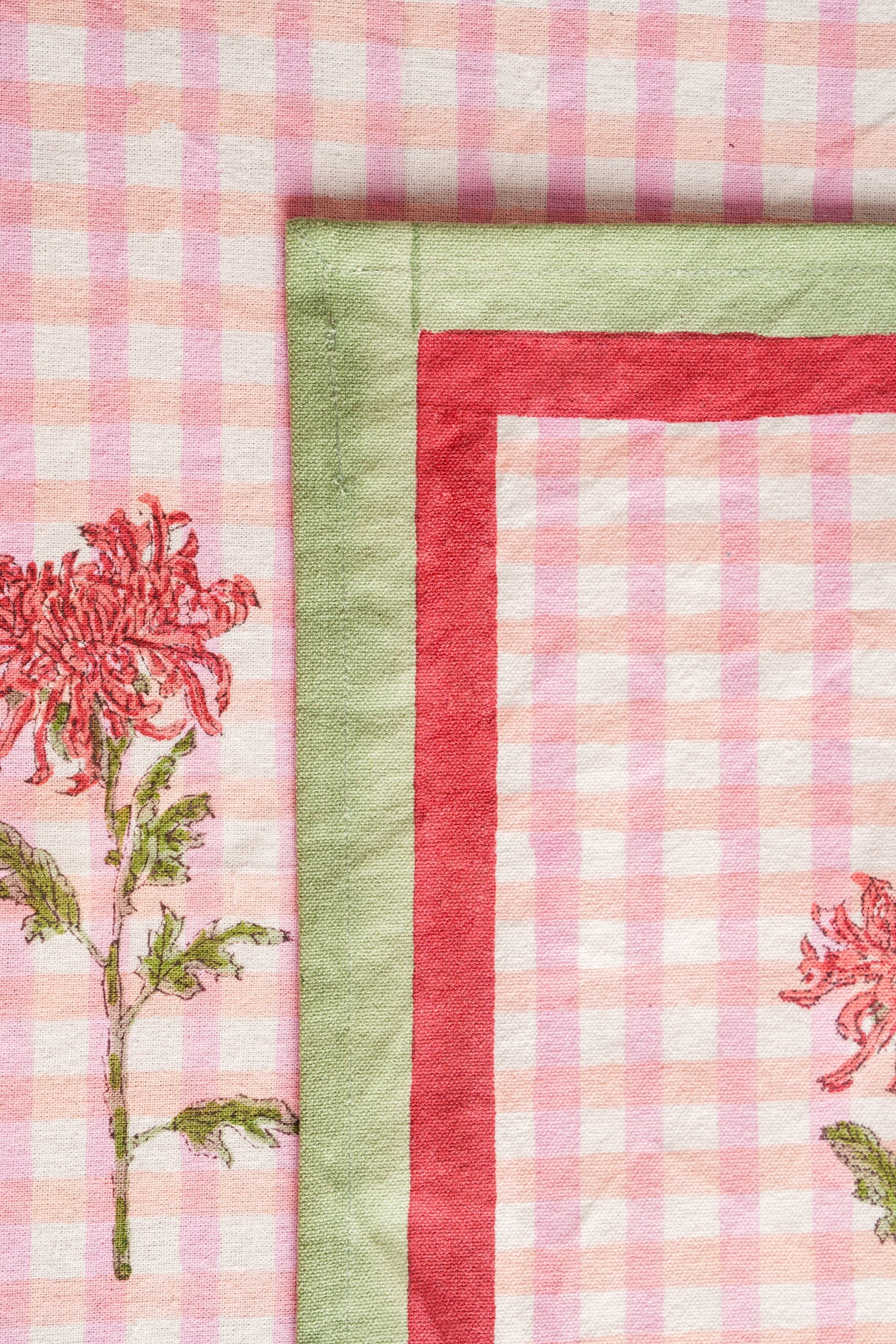 Pink gingham placemat close-up with red border, green edge, and floral blockprint