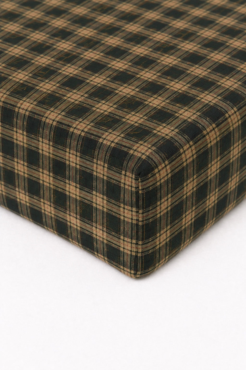 Green and dark plaid crib sheet fitted over a mattress corner
