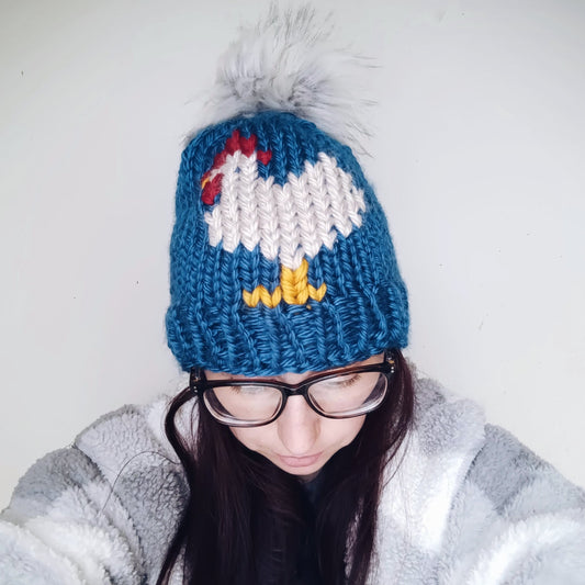 Chicken intarsia knit beanie, blue with white and red pattern, with gray pom-pom