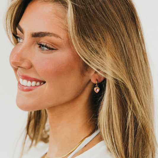 Gold-tone heart dangle earrings with pink heart charm, on ear
