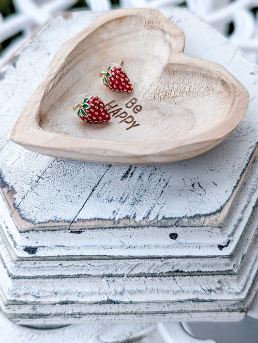 Small red strawberry stud earrings with green leaf caps, paired on heart tray