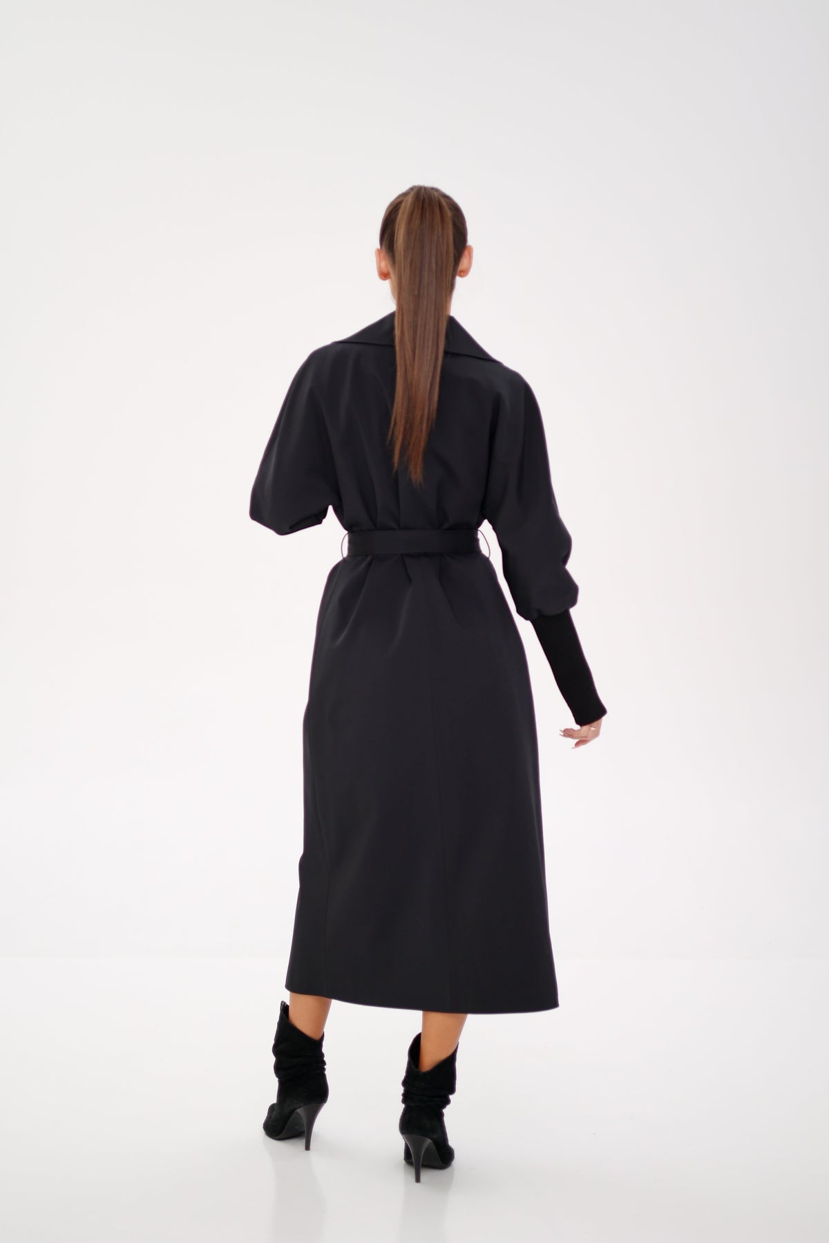 Black trench coat with a belted waist, long length, and wide sleeves, shown from the back