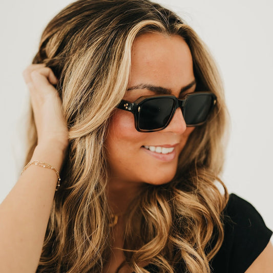 Tortoise-and-black square sunglasses with dark lenses, angled on a smiling woman.