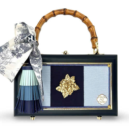 Structured bamboo-handle bag with floral scarf, tassel, and gold floral emblem