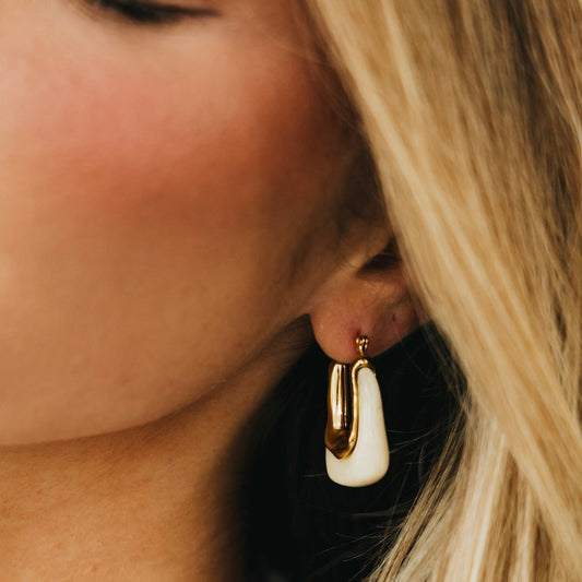Close-up of gold-tone resin hoop earrings with white inner drop and post backing