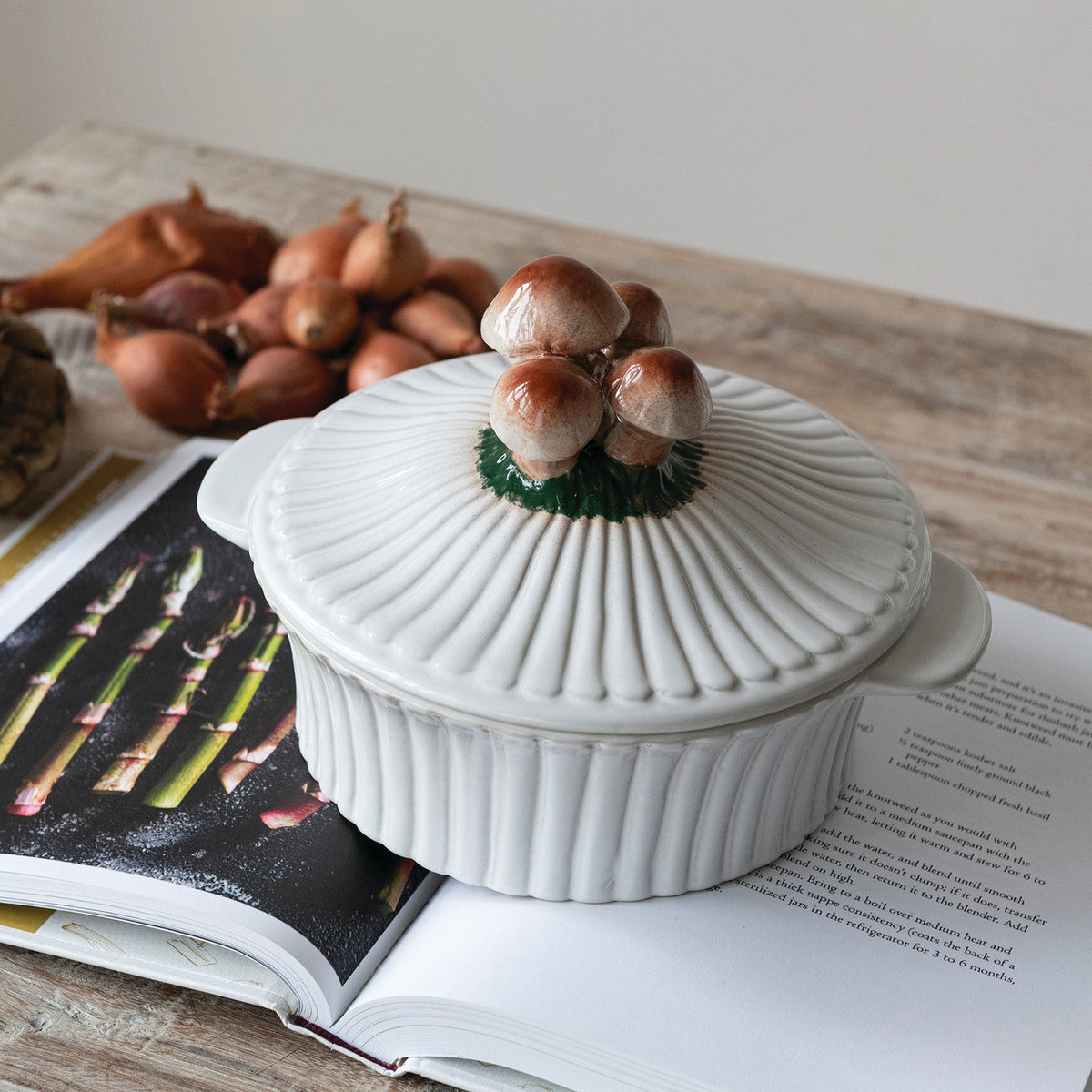 White ceramic fluted baker with mushroom lid, resting on an open cookbook