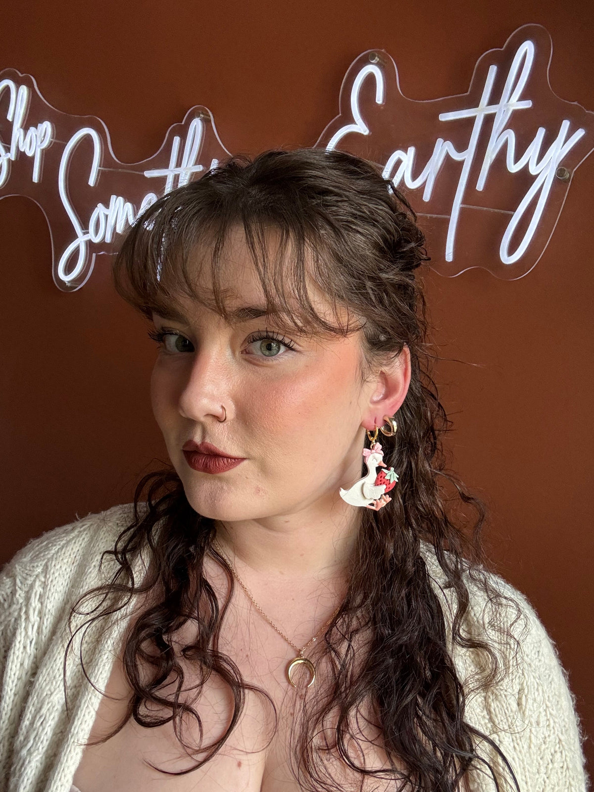 Goose and strawberry drop earrings worn by woman, gold-tone hoops