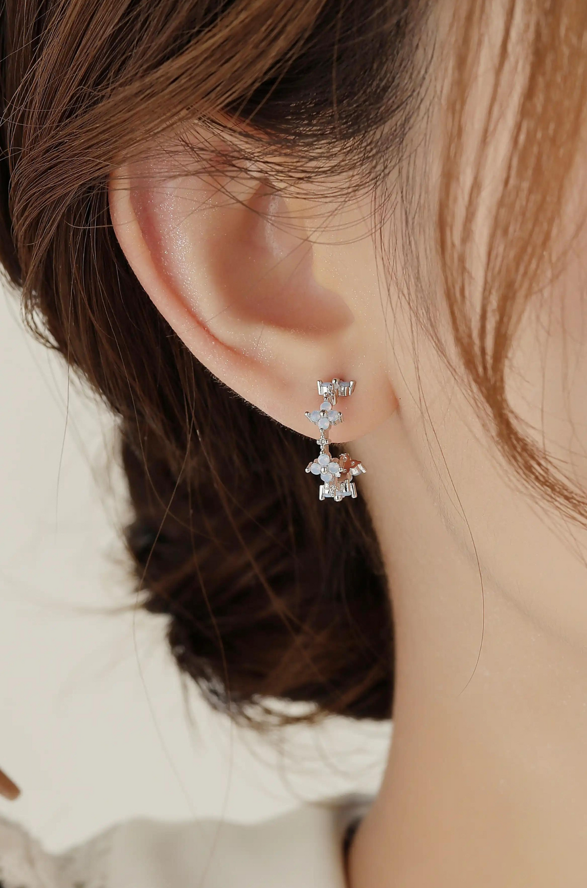 White gold flower hoop earring with pale blue stones, shown worn