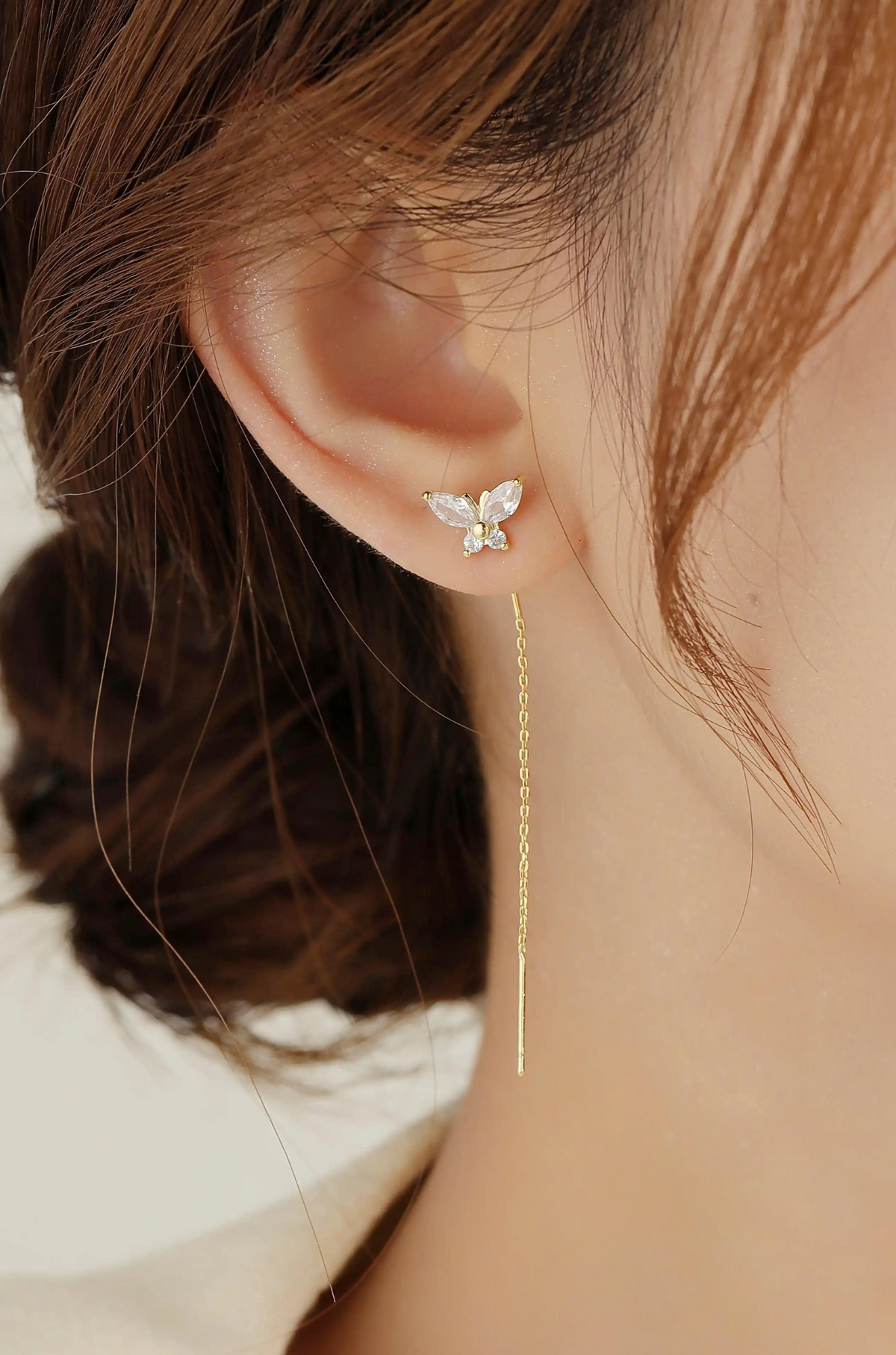 Gold butterfly earring with crystal wings and a long, delicate chain drop, worn on the ear