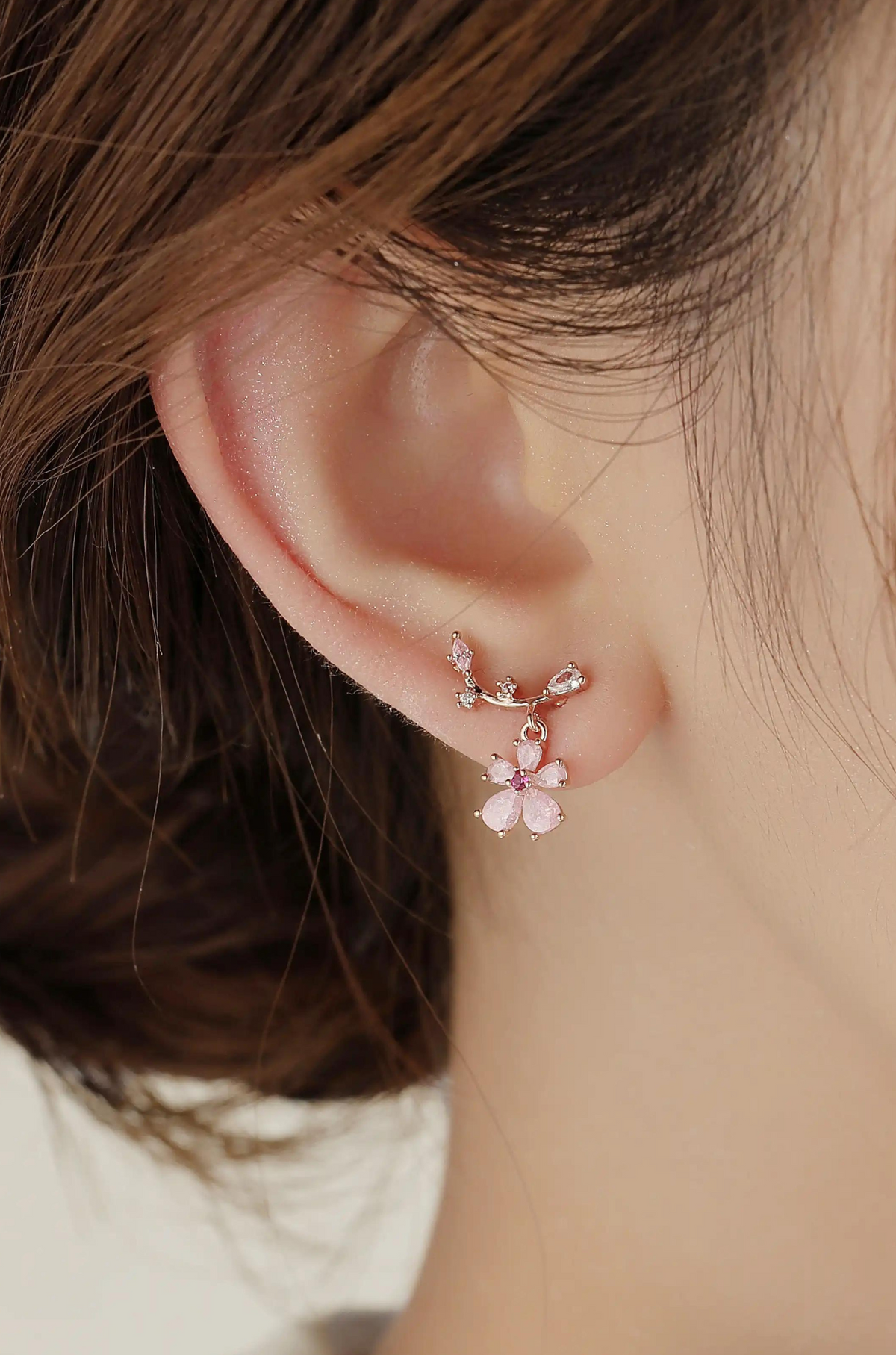 Pink flower drop earring worn on an ear, with a rose gold-tone branch and stone accents