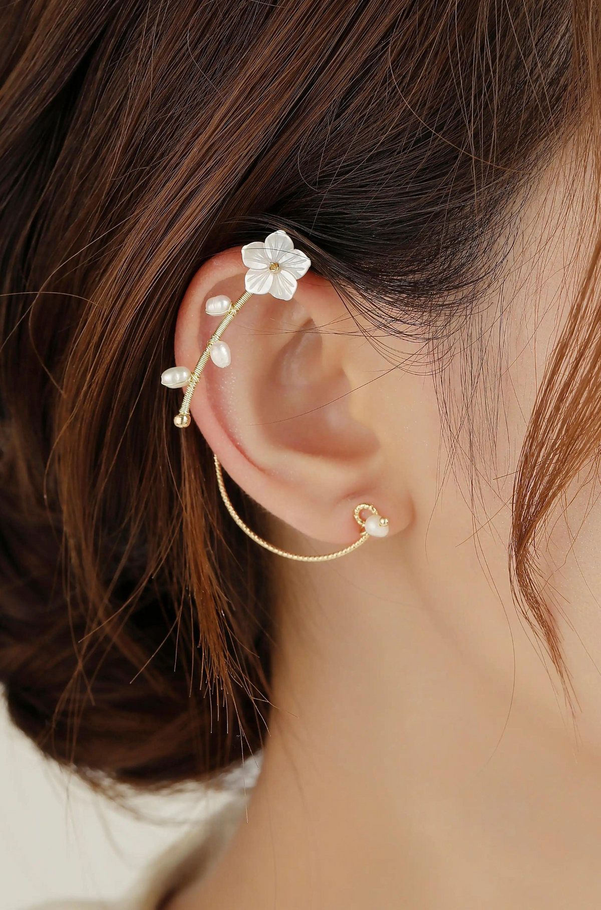 Gold-tone ear cuff worn on the ear, with a white flower and pearl accents