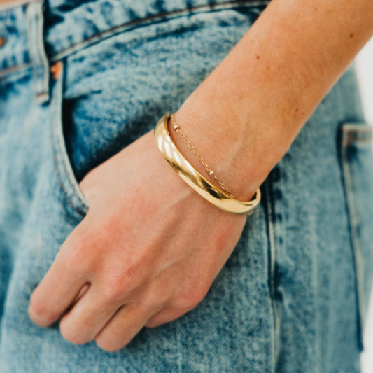 Gold-tone hinged bangle bracelet on hand, smooth polished shine